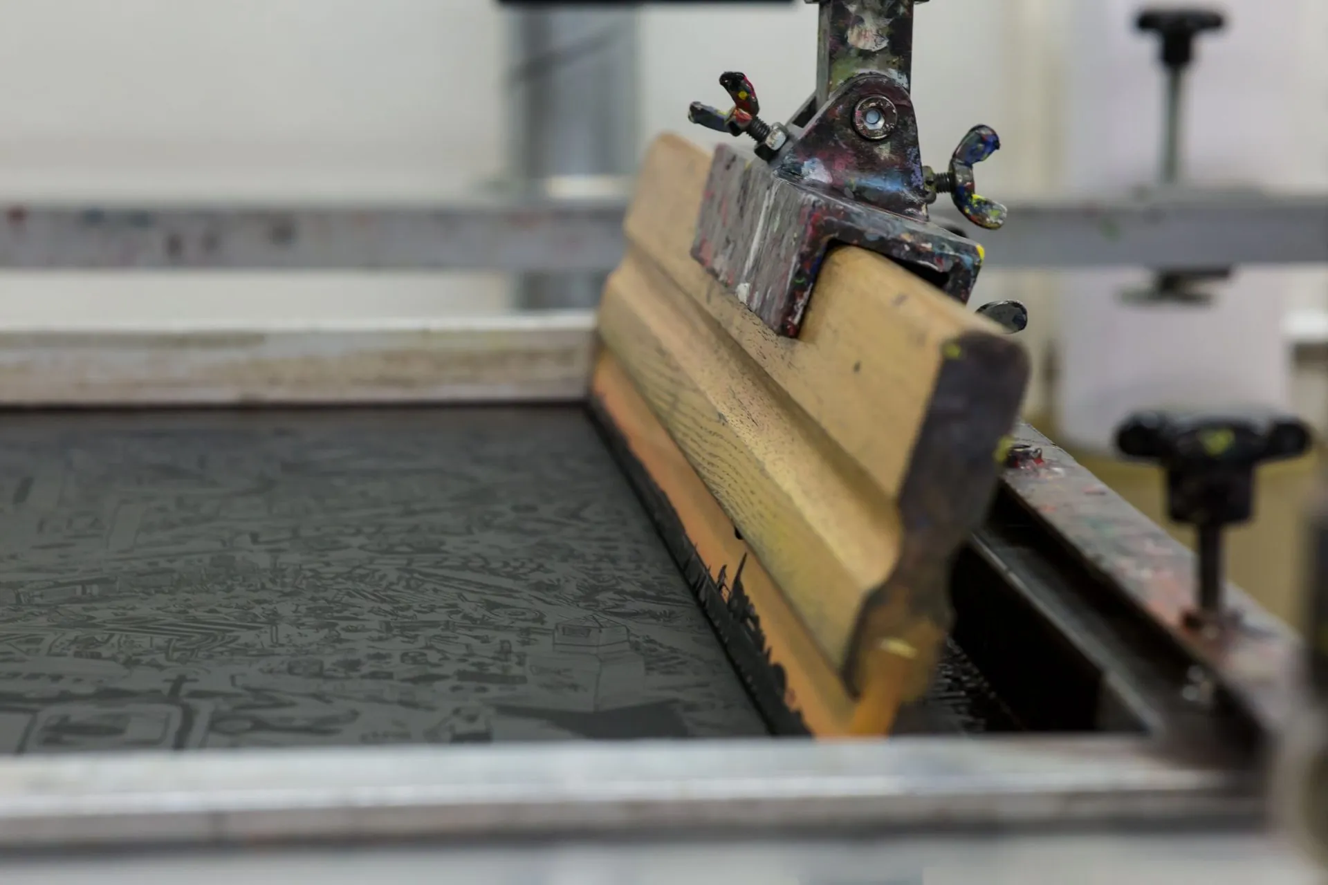 Screen printing squeegee resting on a mesh frame, print-on-demand sportswear