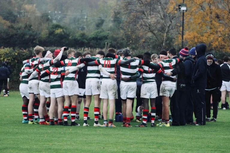 Rugby team in a huddle on a grass pitch in autumn, teamwear in Europe
