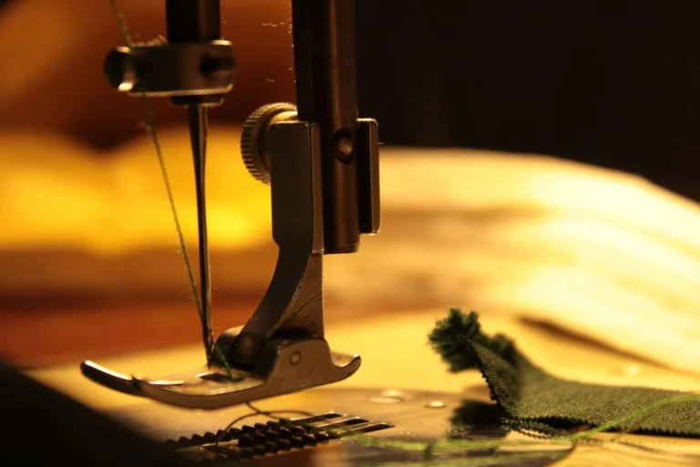 Close-up of a sewing machine needle stitching green fabric under warm light, on-demand manufacturing