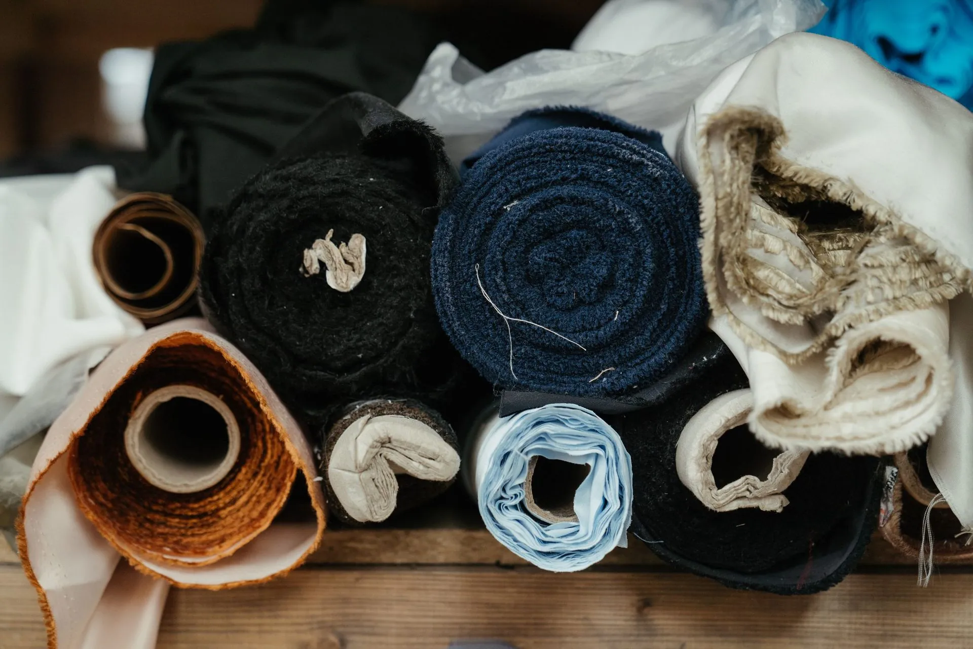 Rolls of assorted fabrics stacked on a wooden shelf, low-waste sportswear production