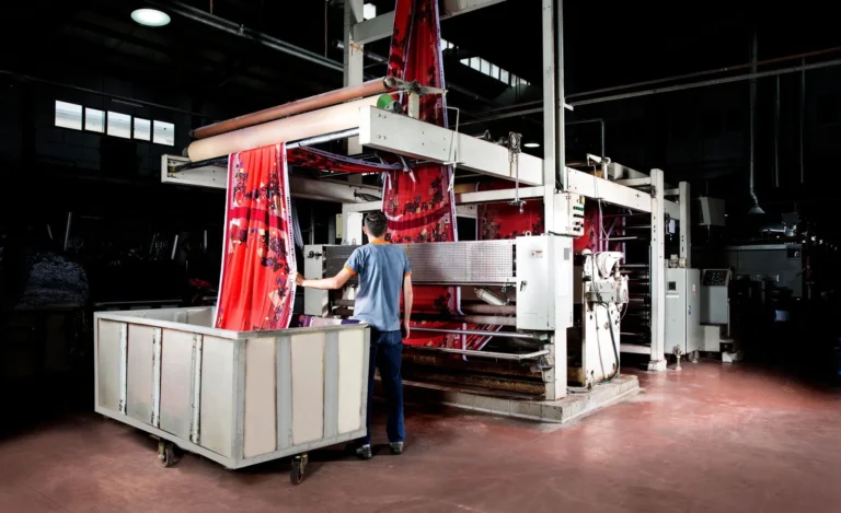 Industrial textile machine running red printed fabric in a dark production hall