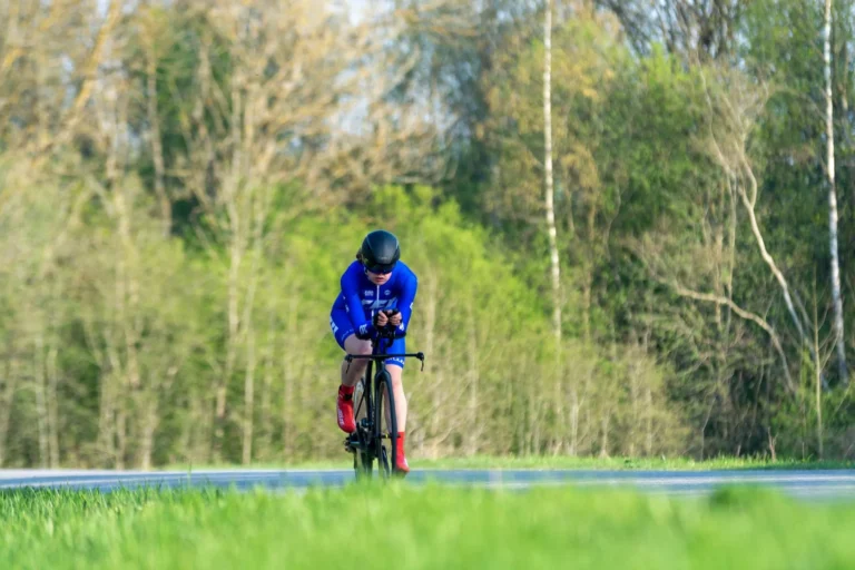 Cyclist in a time-trial position riding past spring woodland, cycling shorts in use
