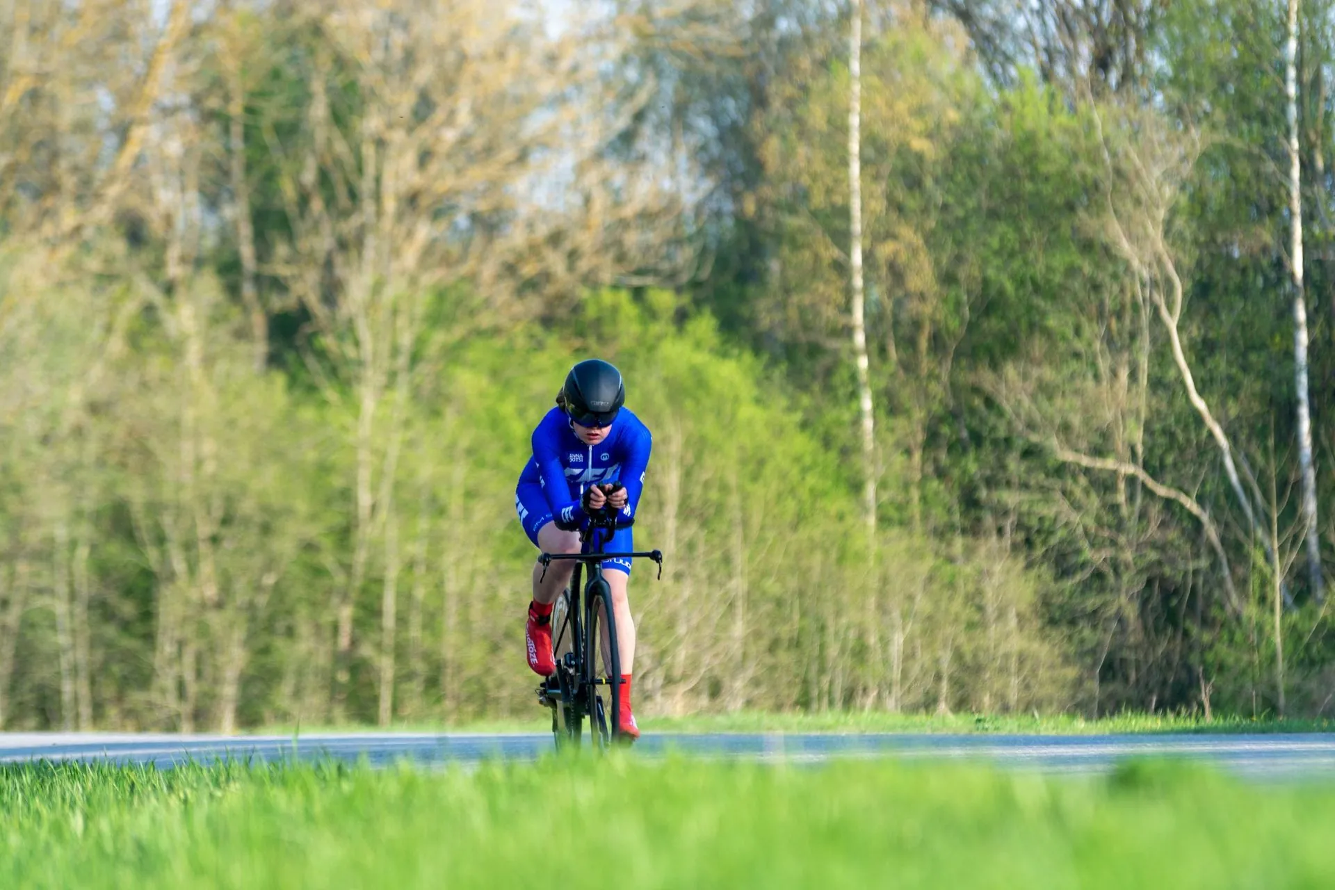 Cyclist in a time-trial position riding past spring woodland, cycling shorts in use