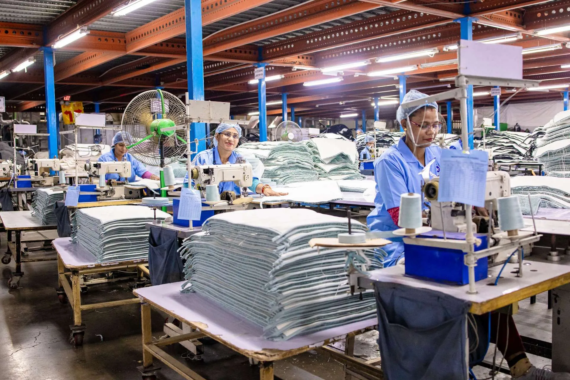 Garment workers at sewing stations in a large production hall, future of sportswear production