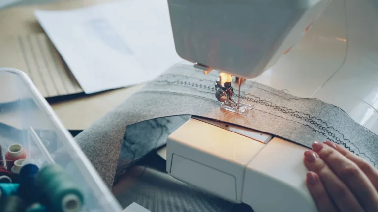 Sewing machine stitching grey fabric beside thread spools, small-batch custom sportswear production