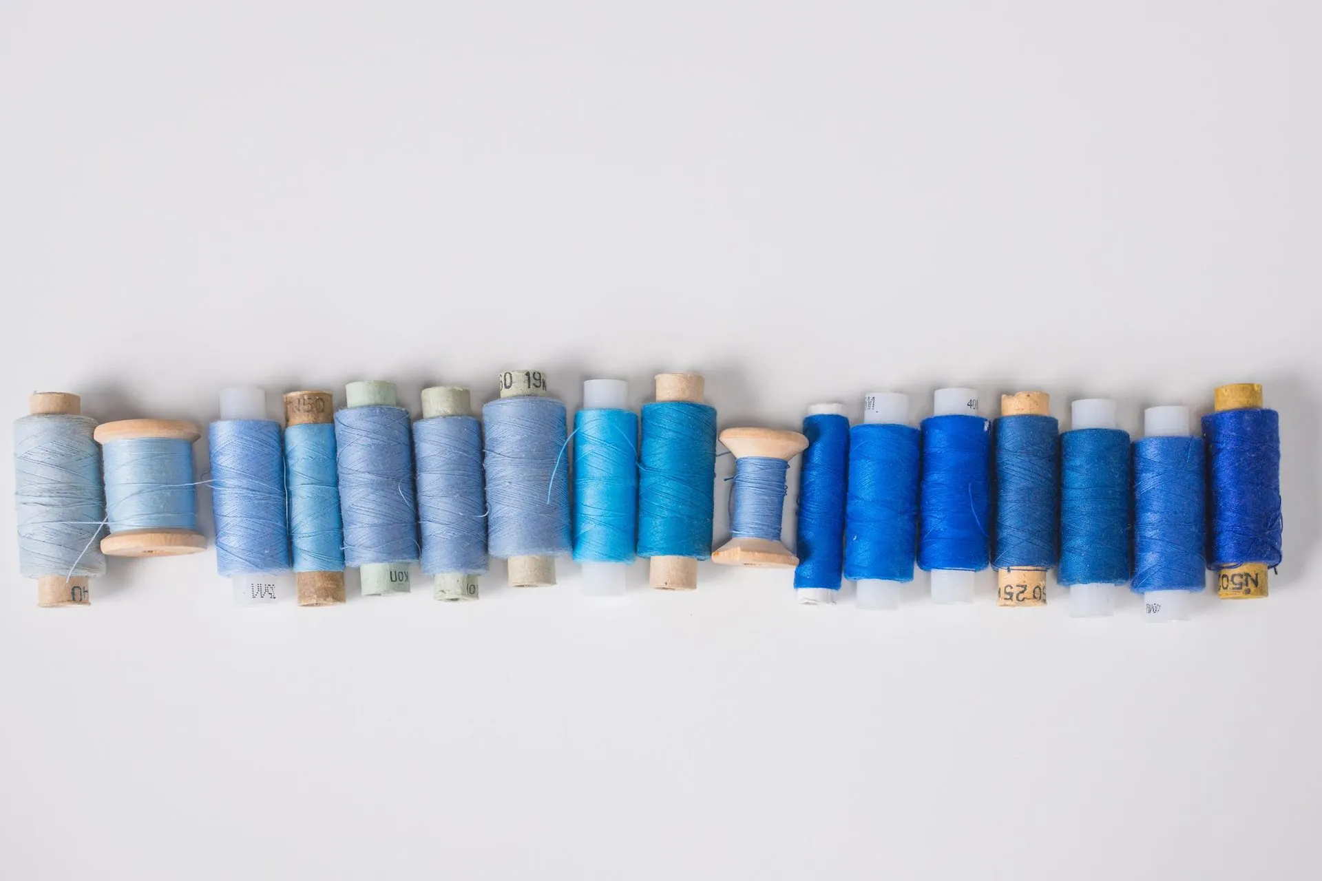 Row of thread spools in a blue gradient on white, craftsmanship in sportswear