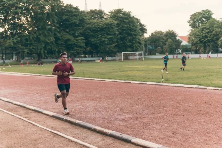 Runner training on a red track near a football field, polyester sportswear and odour