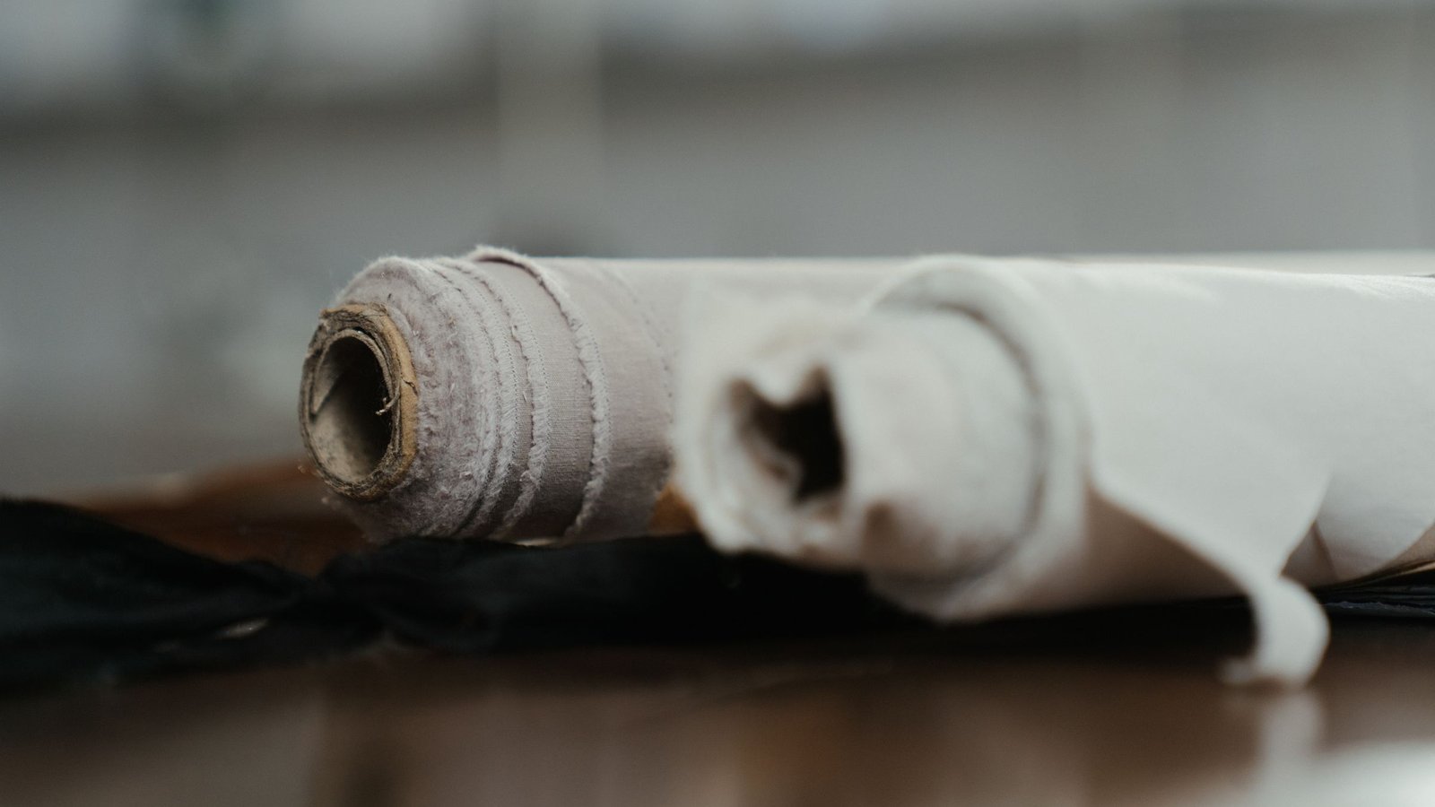 Two rolls of light fabric lying on a dark wooden workshop table