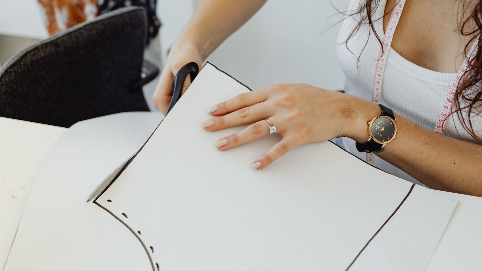 Hands cutting a paper garment pattern with scissors on a work table