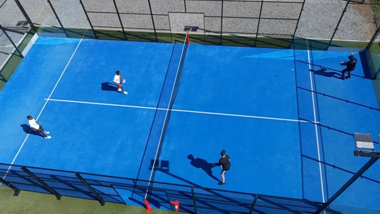 Aerial view of four players in a doubles match on a blue outdoor padel court, the setting padel brands design apparel for