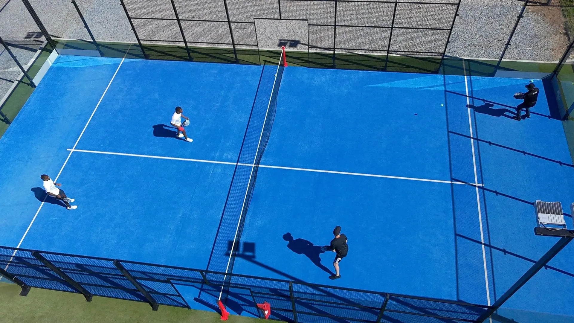 Aerial view of four players in a doubles match on a blue outdoor padel court, the setting padel brands design apparel for
