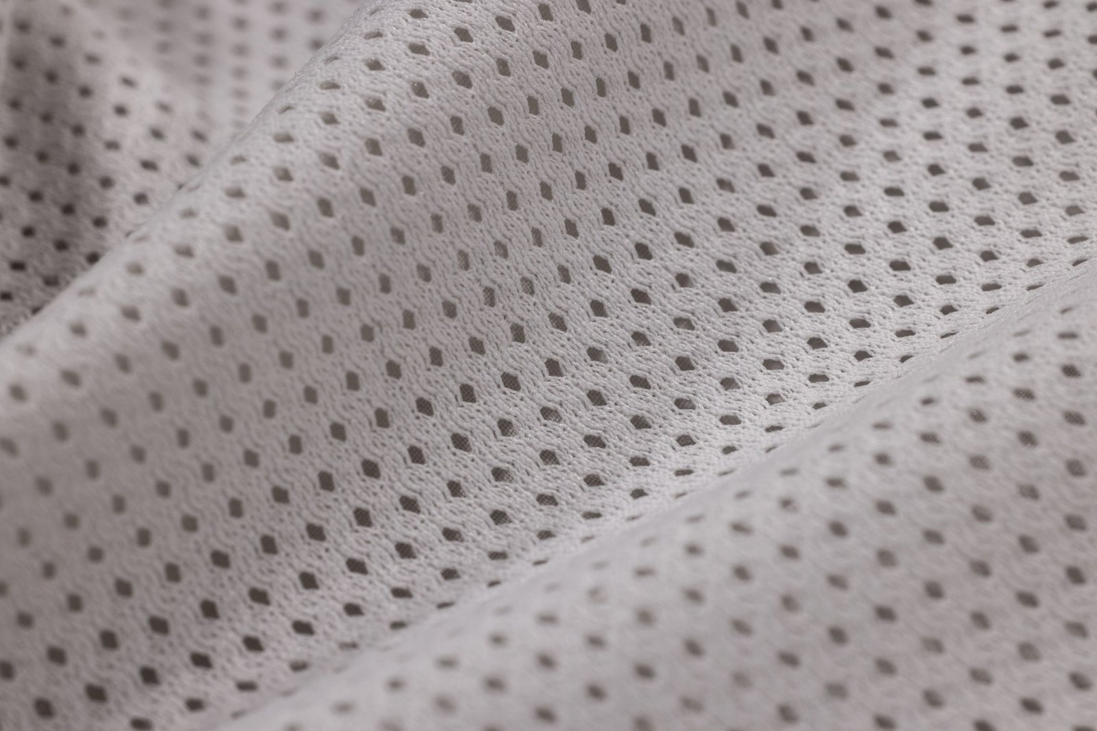 Macro of white sportswear mesh fabric with small regular holes, folded in soft light