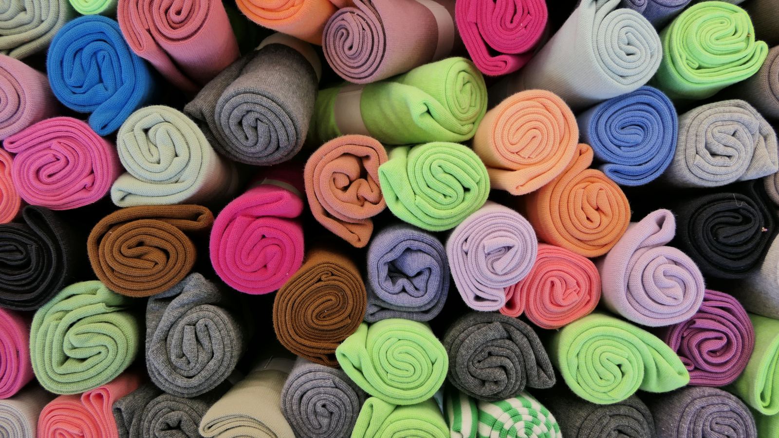 Rolls of knitted fabric in many colours stacked end-on