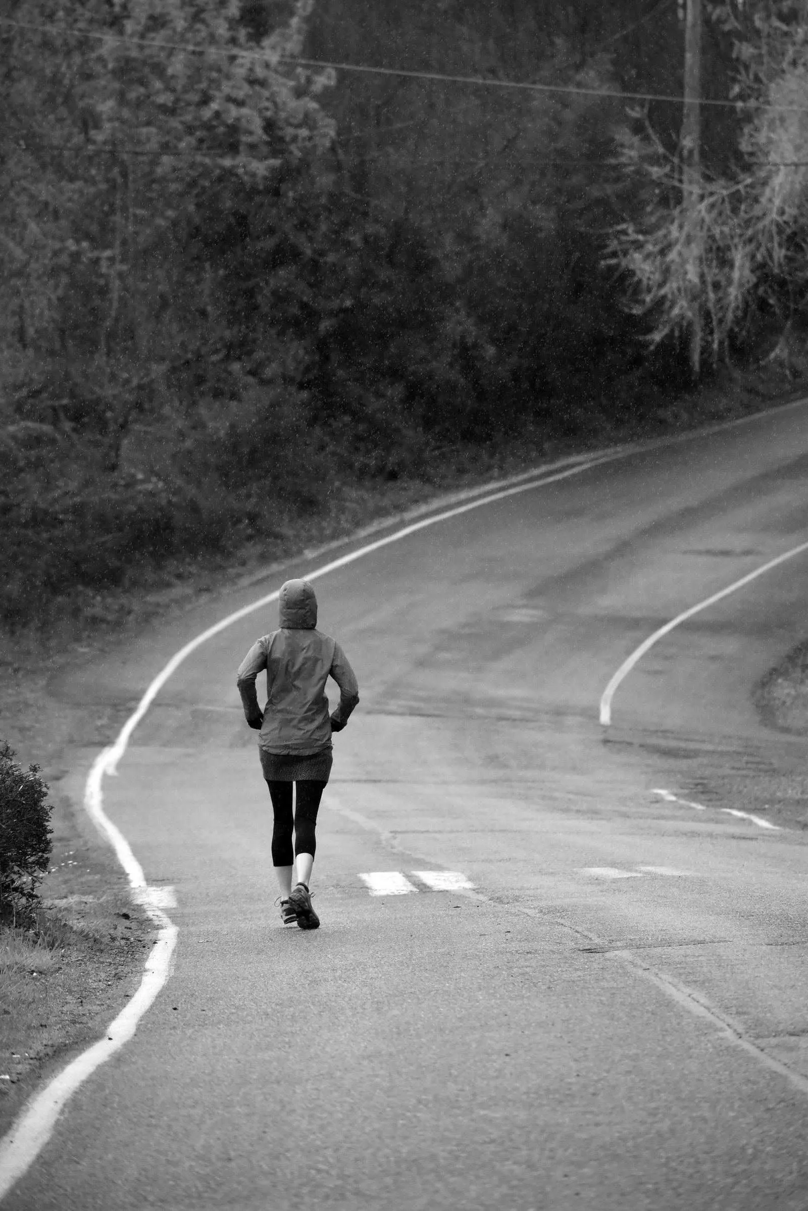 Runner seen from behind on a winding rural road, wearing a hooded running layer
