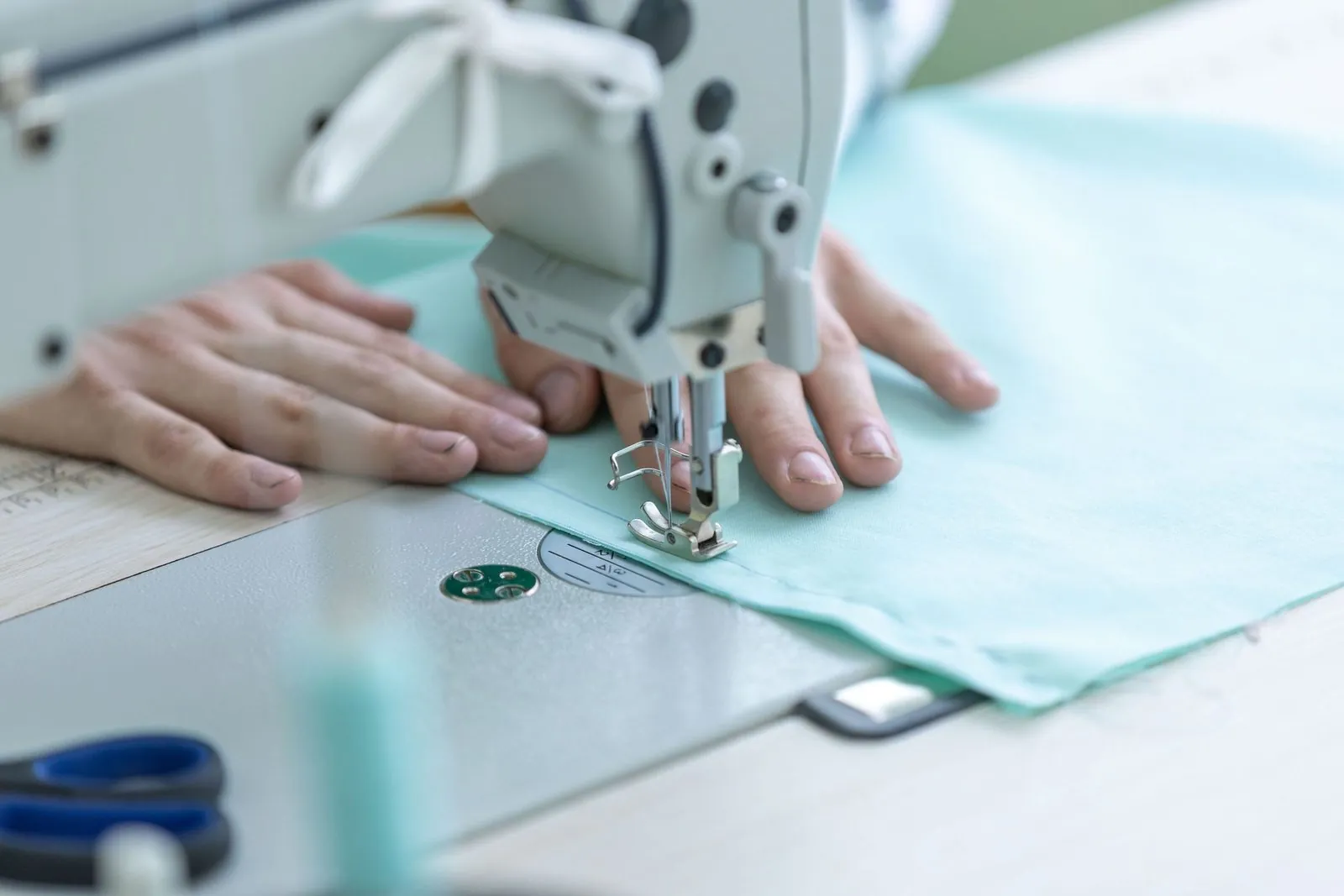 Hands guiding light fabric through a sewing machine, a key step in cycling kit construction