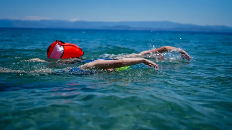 Two open-water swimmers mid-stroke in clear blue sea, the setting swim and surf brands design rashguards for