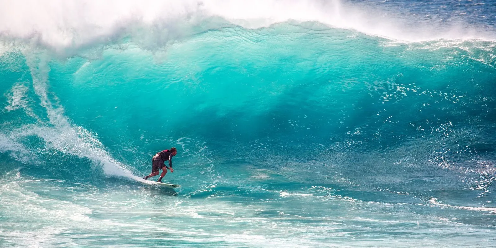 Surfer riding a turquoise ocean wave, the kind of use a first swim rashguard drop is built for