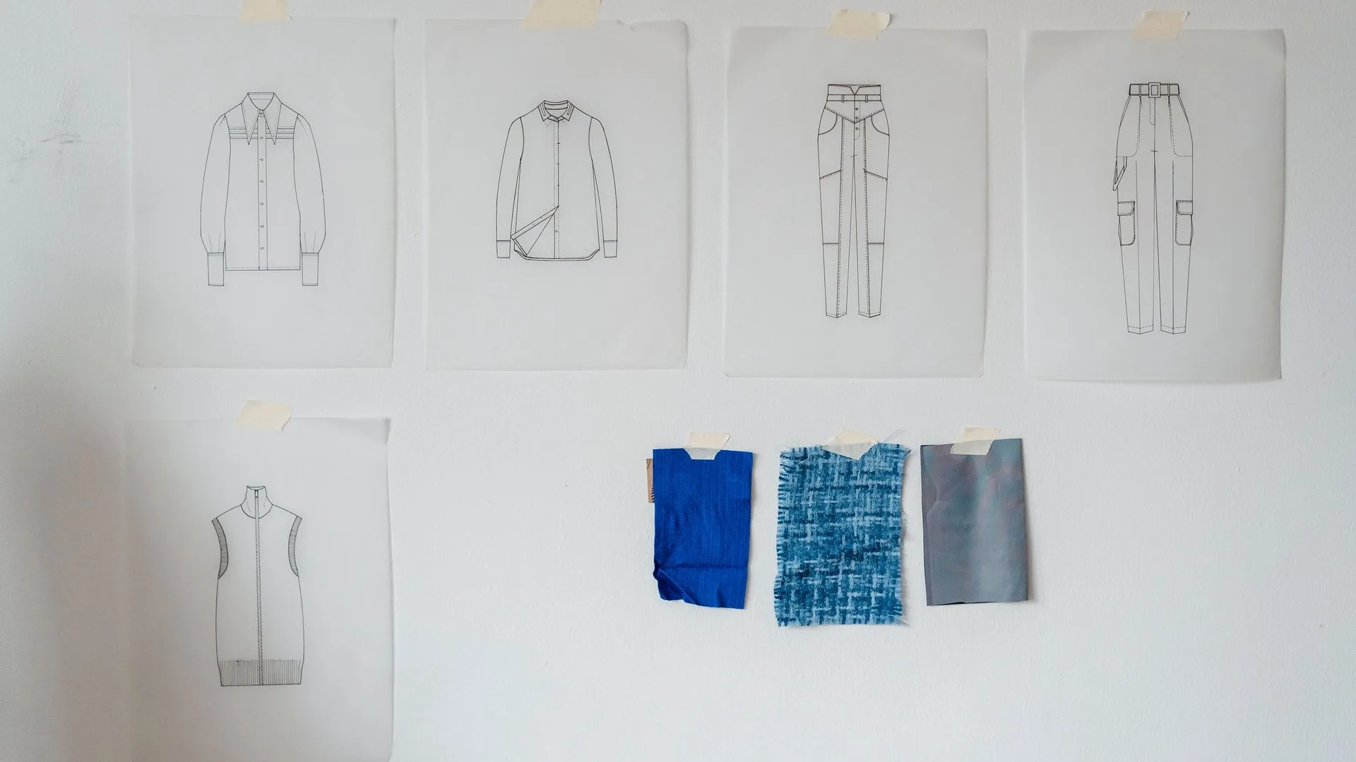 Flat technical sketches of garments taped to a studio wall above three fabric swatches, the starting point of a rashguard tech pack