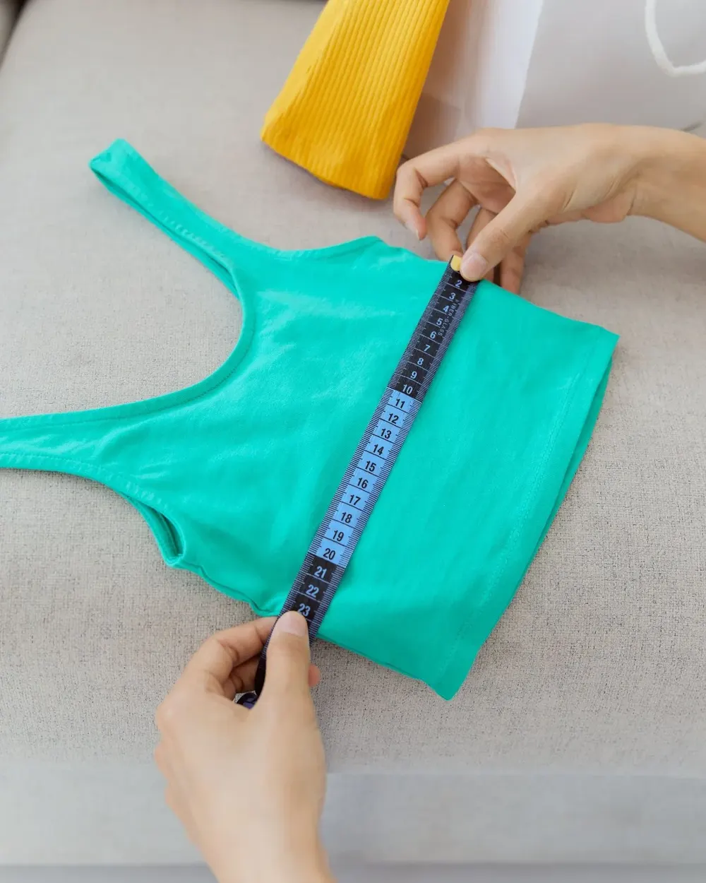 Hands measuring the width of a stretch top laid flat with a tape measure