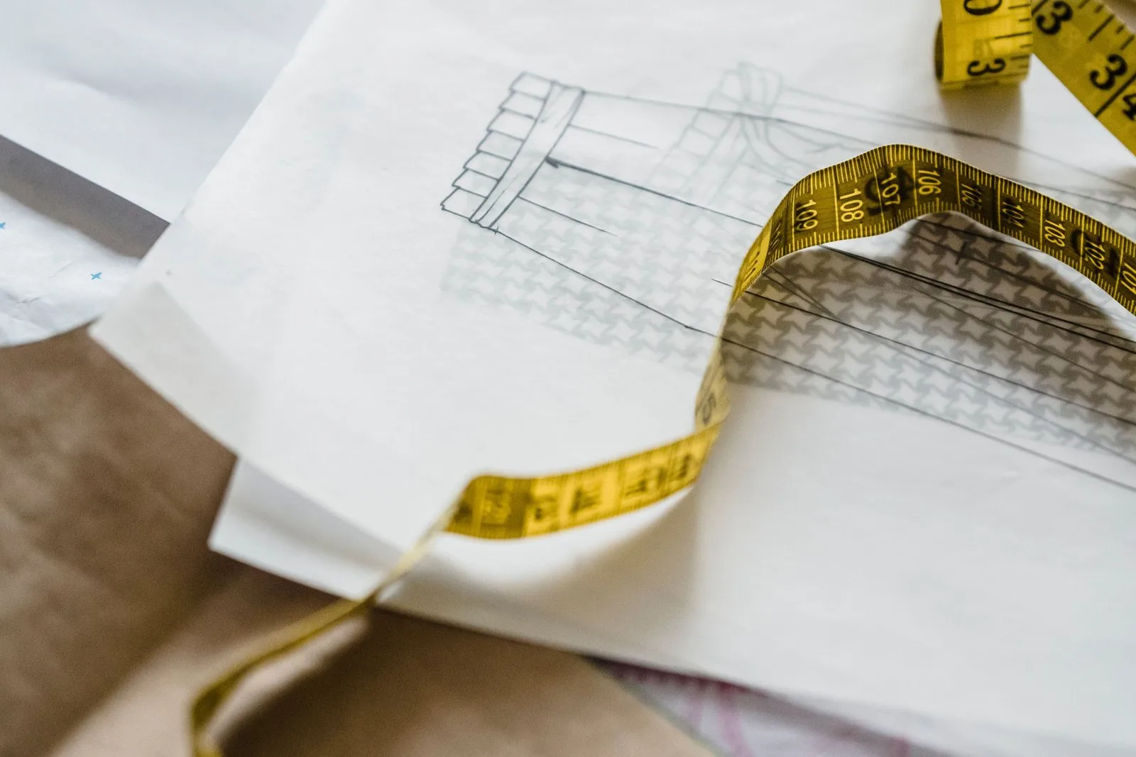 Yellow tape measure lying across a pencil garment sketch on a pattern table