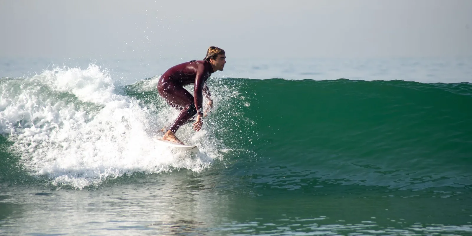 Surfer in a full-length suit riding a breaking wave in clear sea